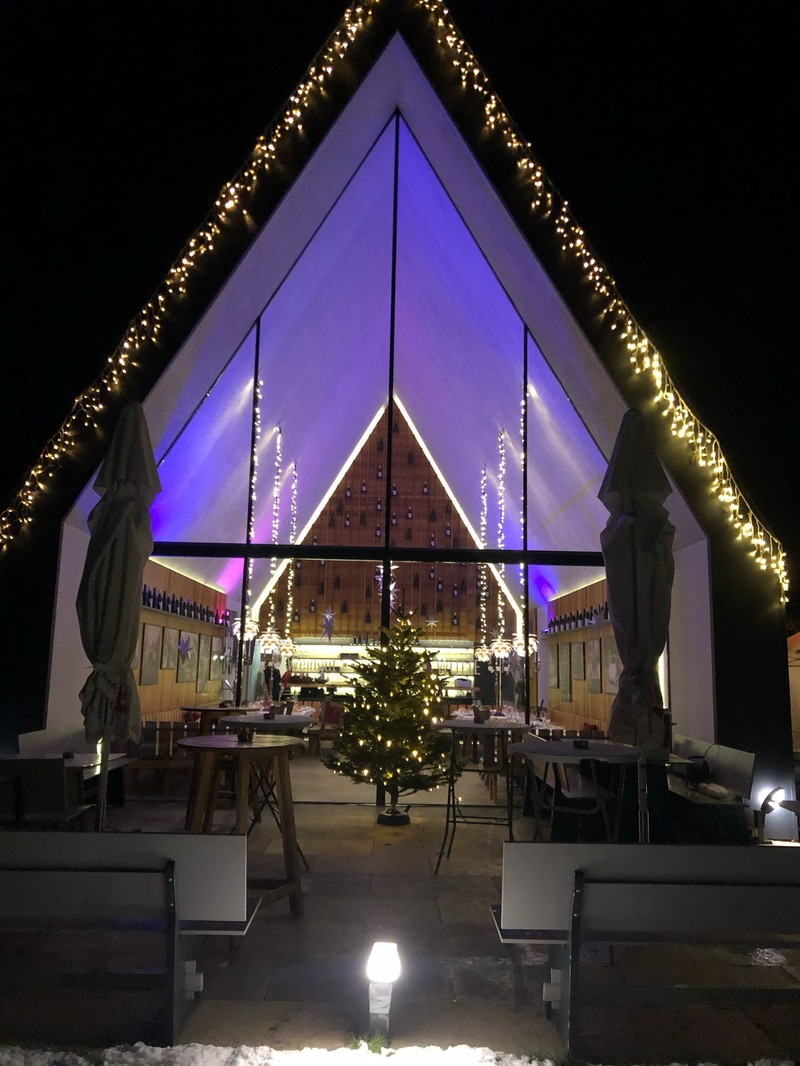 Winterliche Ansicht des Buschenschanks Wutte mit beleuchtetem Giebeldach und Weihnachtsbaum vor dem Eingang